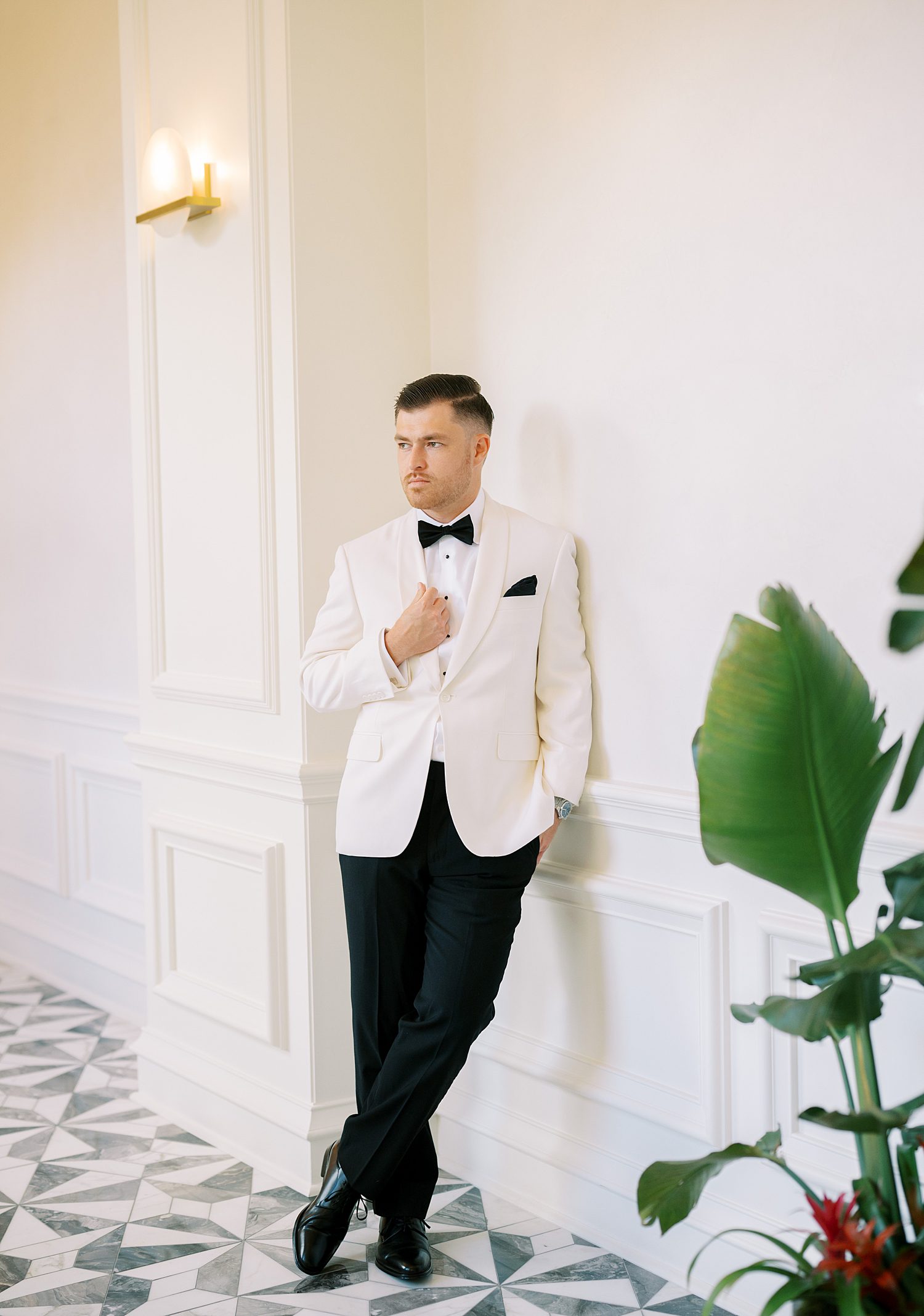 groom in white tux with black lapels leans on wall inside the Ritz Carlton Sarasota