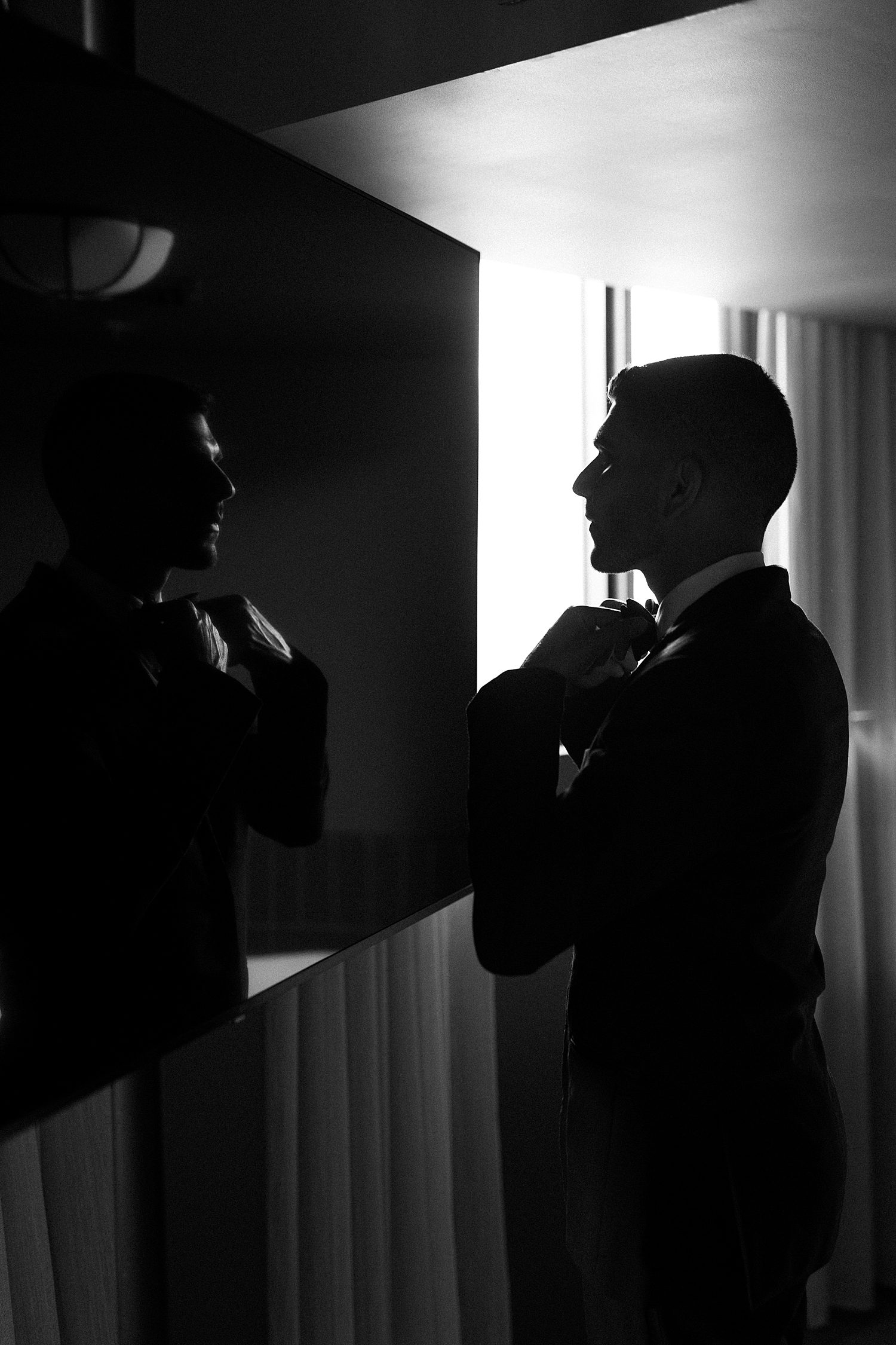 black and white photo of groom tying tie in mirror