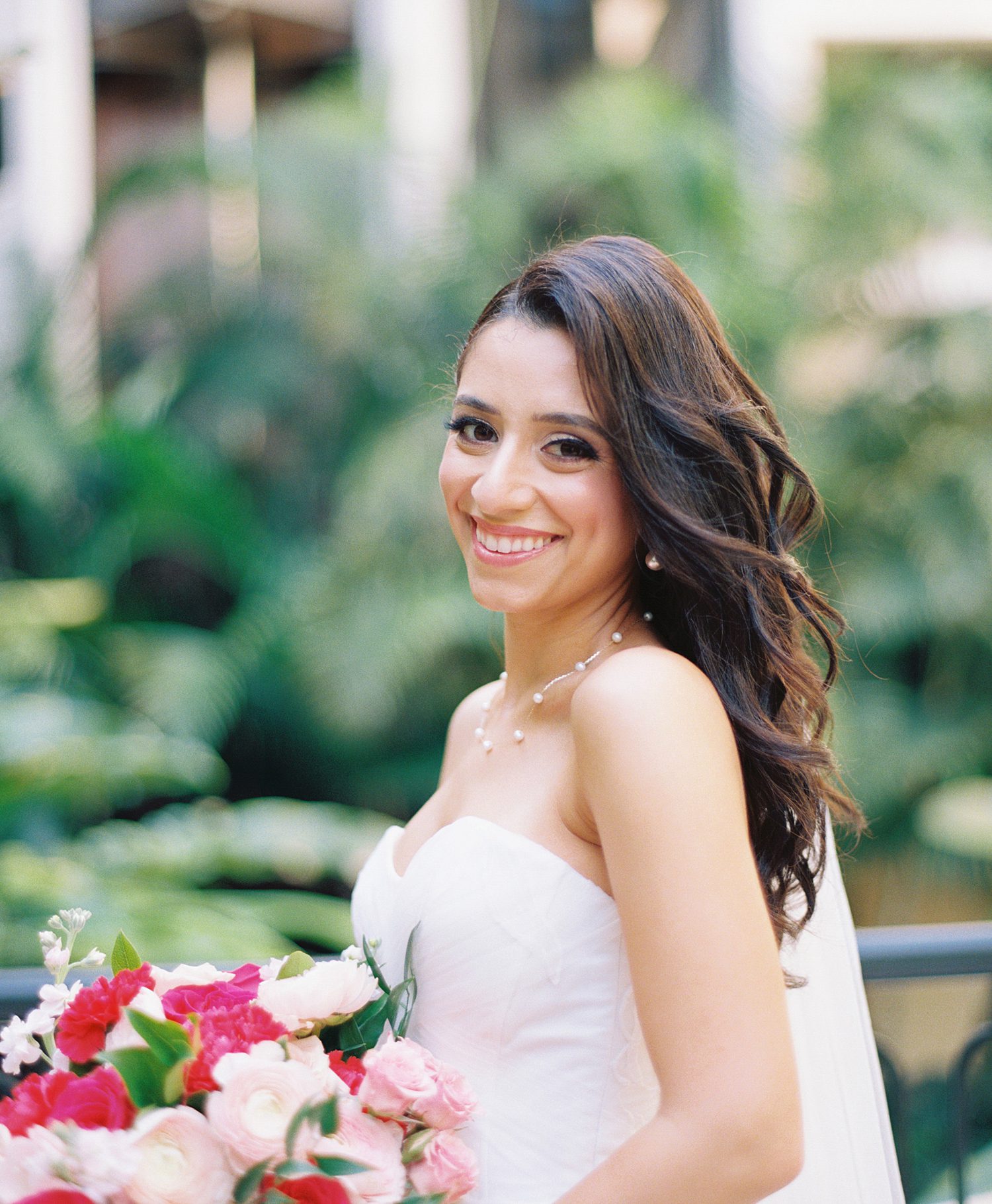 bride smiles holding bouquet of pink and red flowers in atrium at Mayfair House in Miami FL