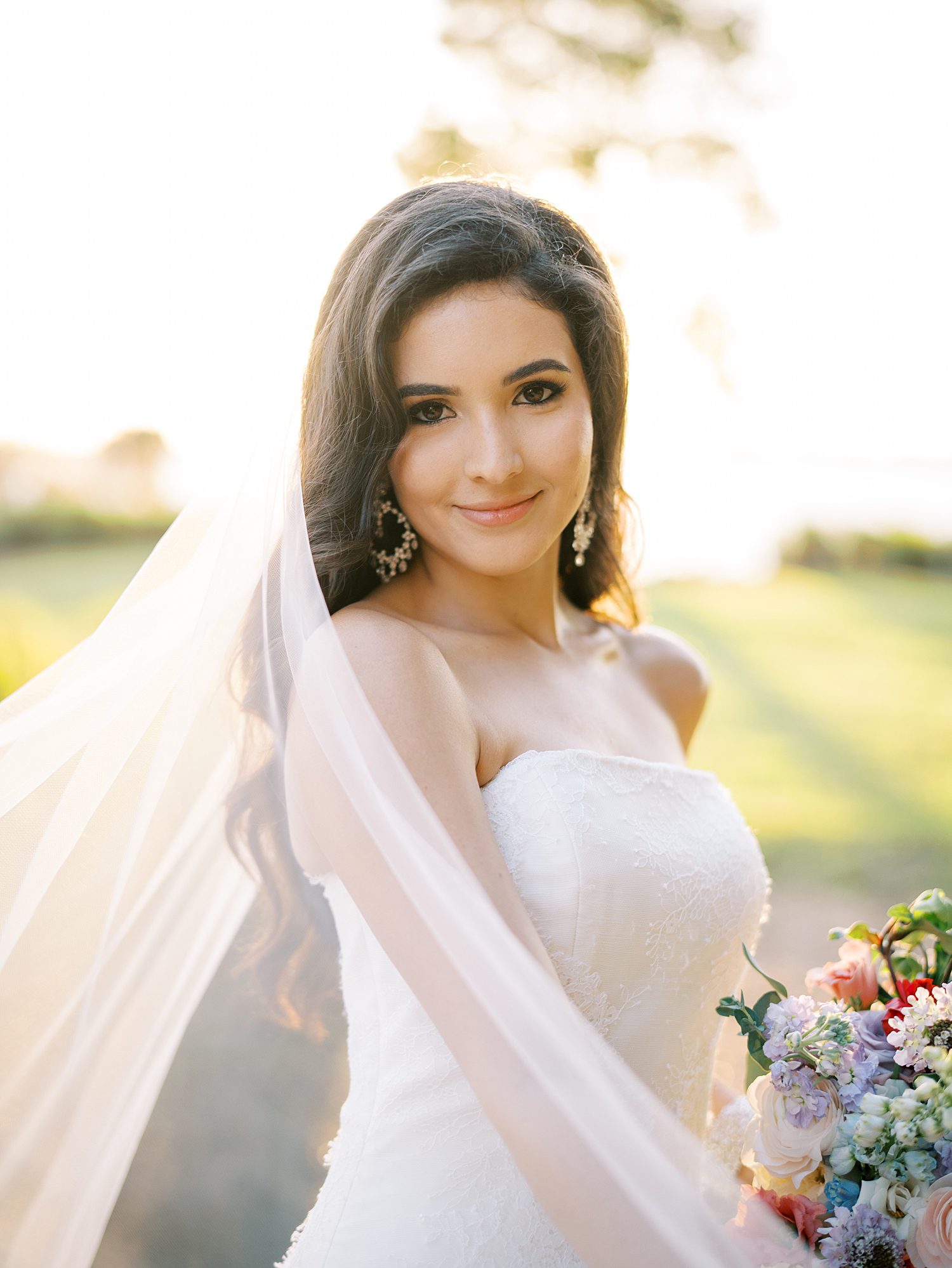bride smiles in strapless gown with veil pulled around her shoulders 