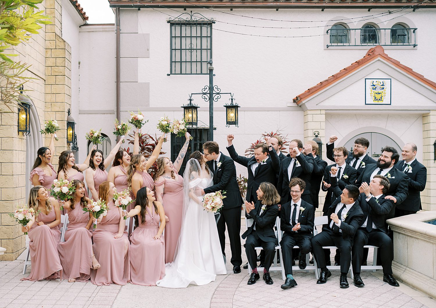bride and groom kiss with wedding party cheering near them