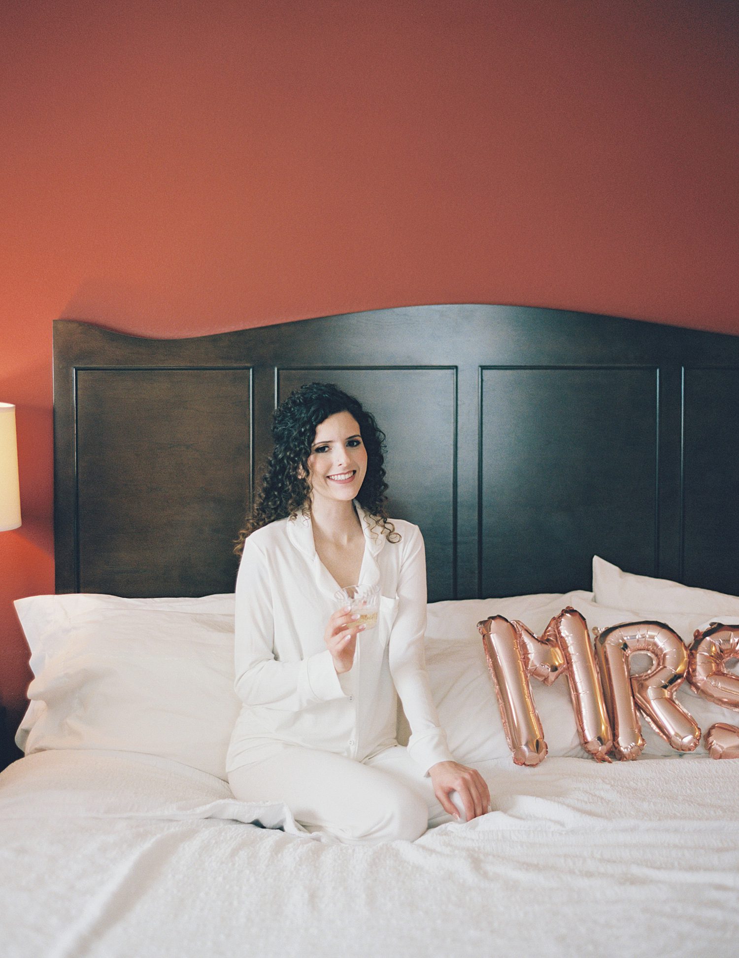 bride sits on bed with MRS balloons in hotel