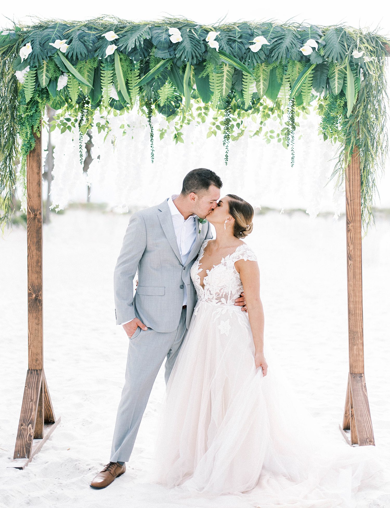 Florida Beach Elopement Guide | Couples kiss under wedding arch decorated with tropical greenery