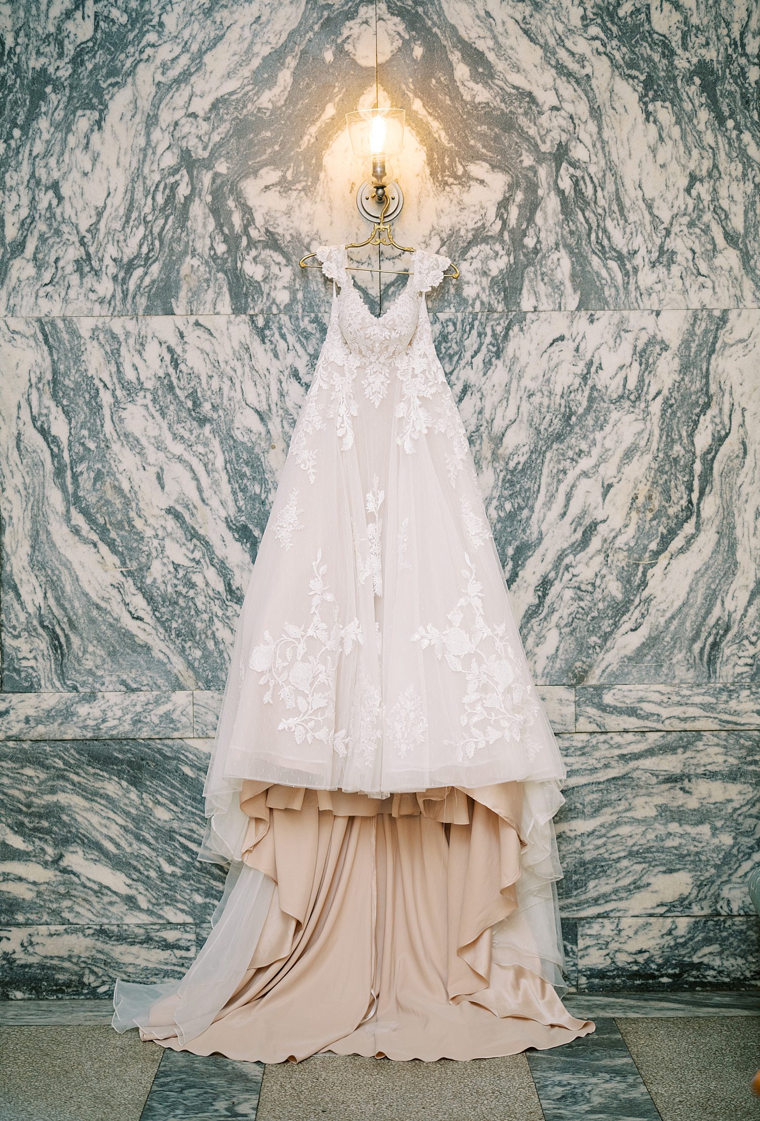 wedding dress hanging against marble wall 