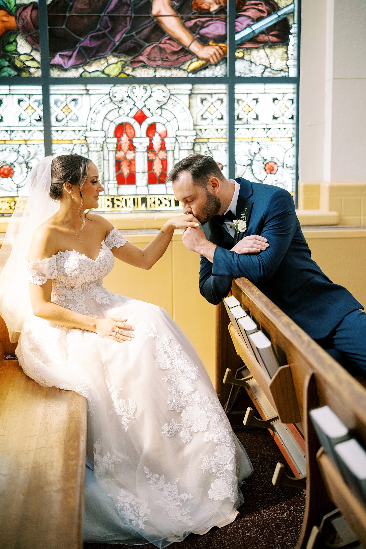 groom kisses bride's hand while sitting in church pew