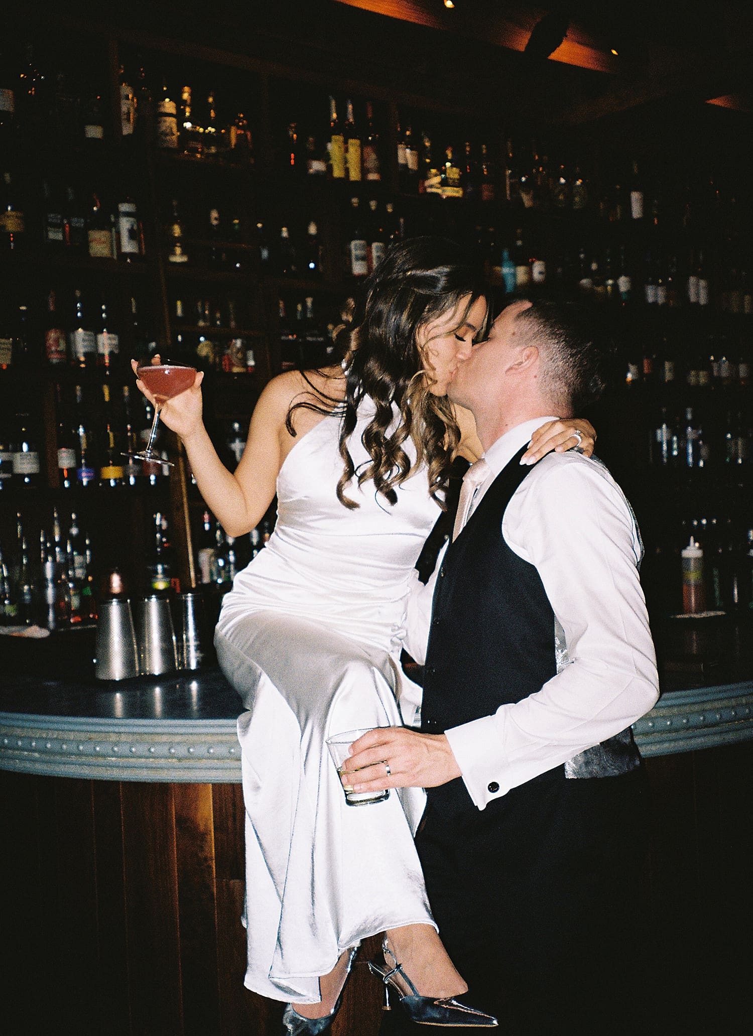 bride sits on bar as groom leans in for a kiss