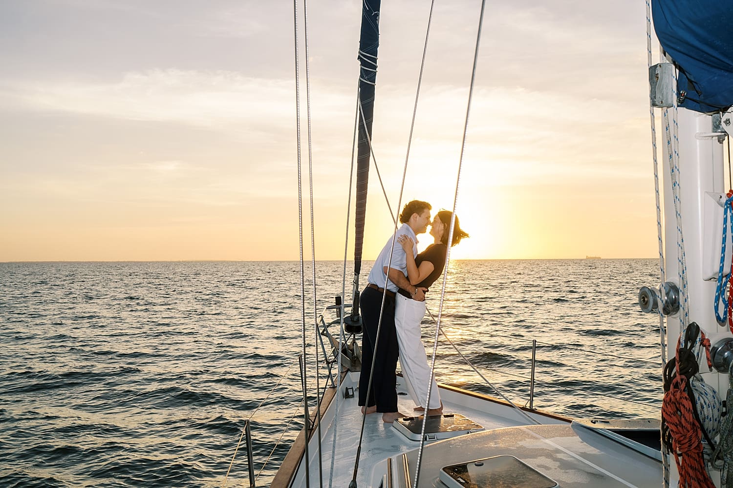couple lean in together while standing on front of sailboat at sunrise