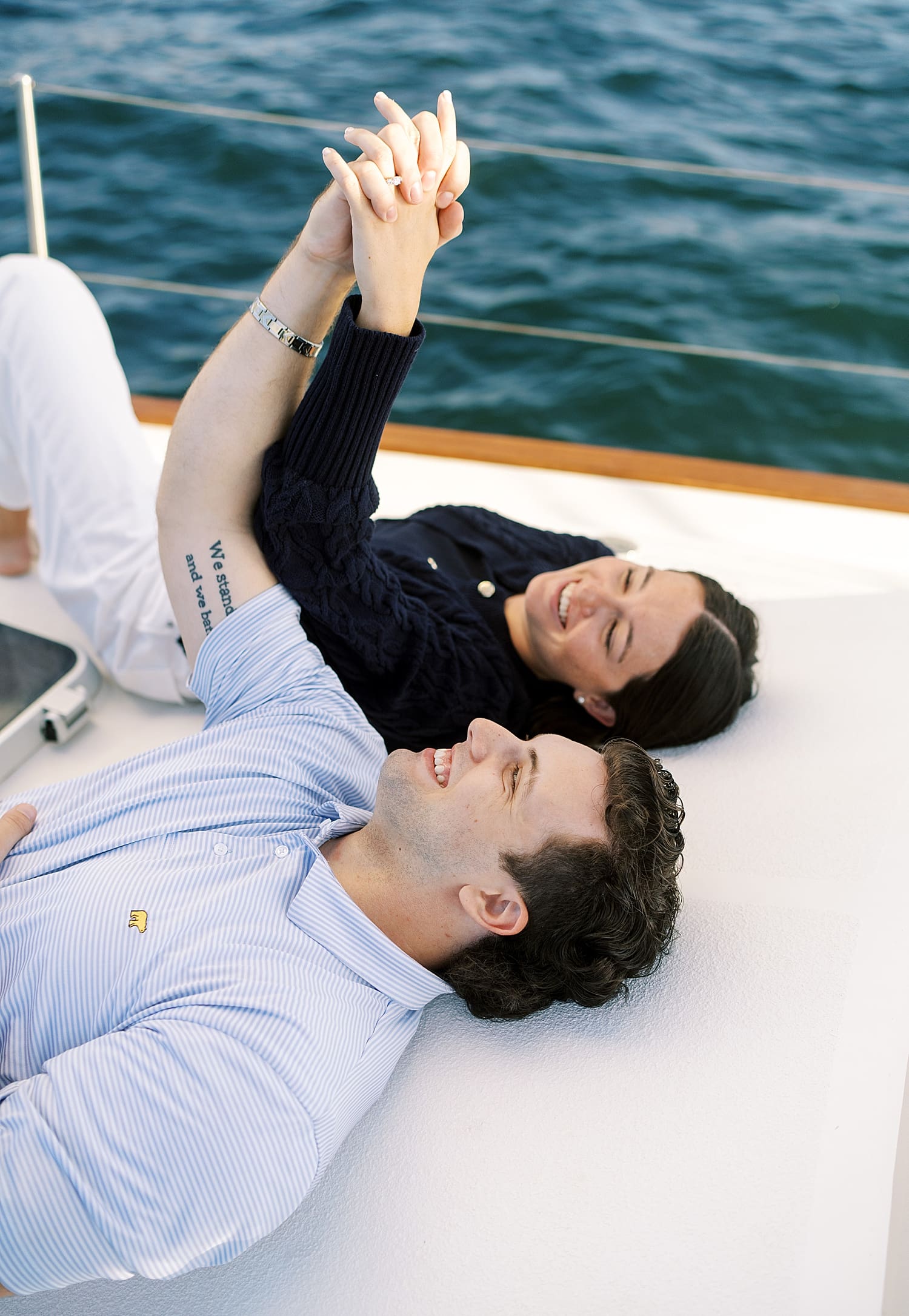 couple lay on front of sailboat and hold hands, laughing together