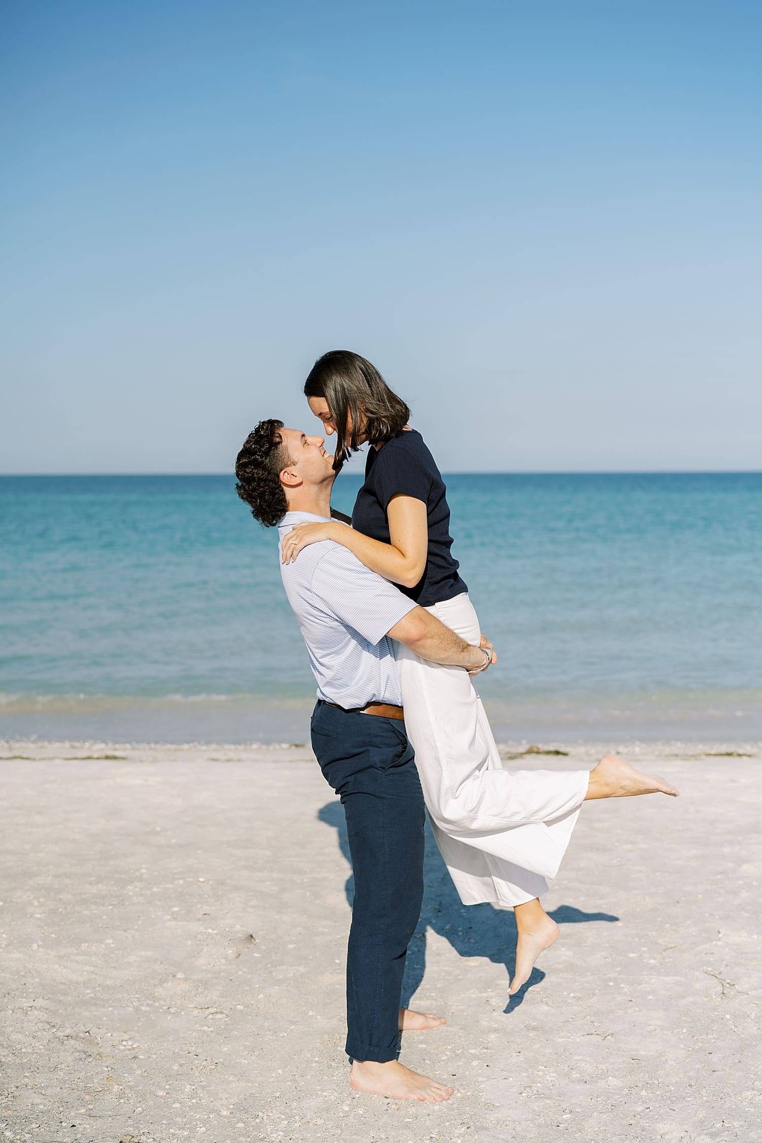 Romanic engagement photos on Tampa beach of man lifting woman up in arms