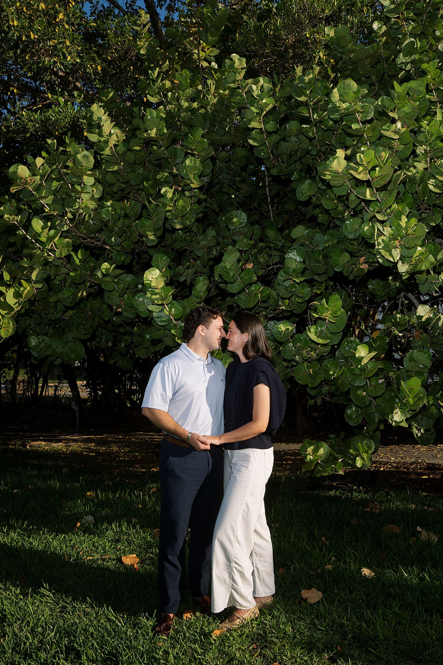 couple lean in to each other by large tree