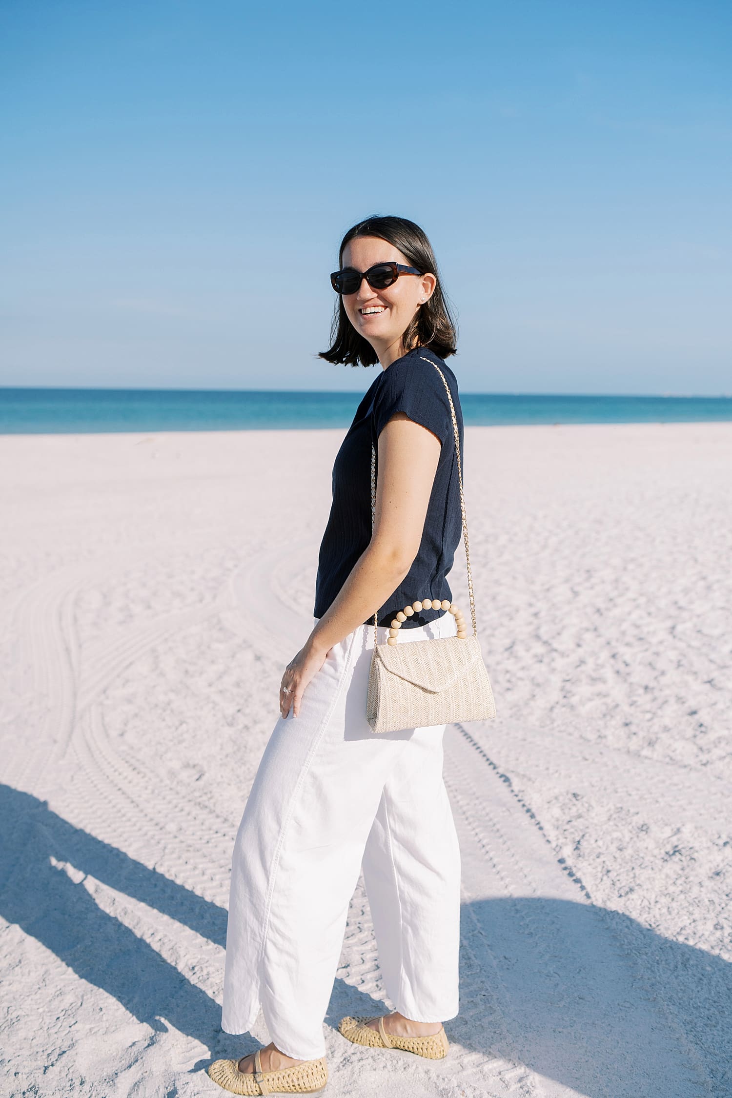 woman on white sand beach with blue waters and clear sky