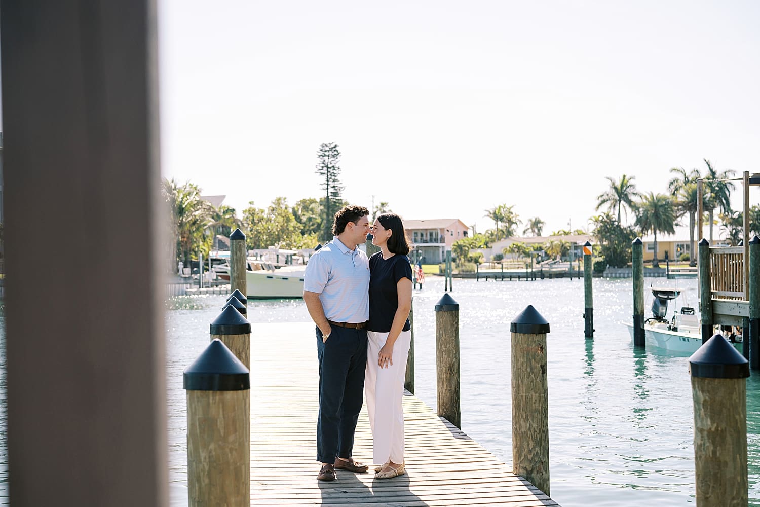 couple kiss on dock by the water during Sunrise Sailboat Engagement Session in Tampa