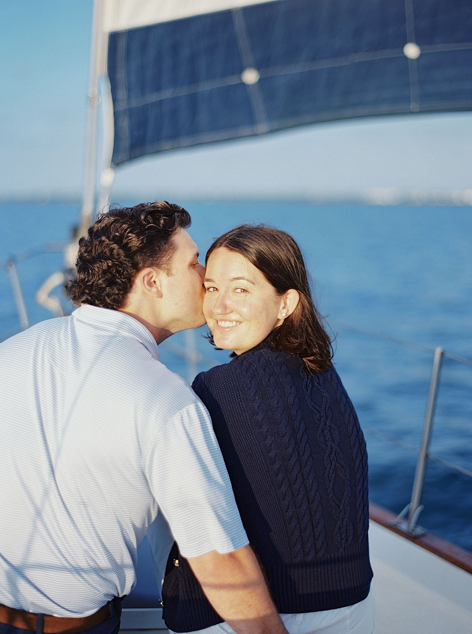man kisses woman's cheek during Florida engagement session on sailboat