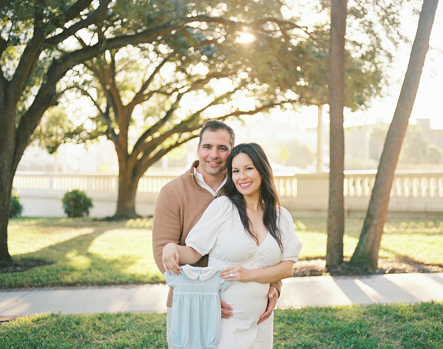 expectant parents hold up blue outfit for baby boy during Tampa maternity session