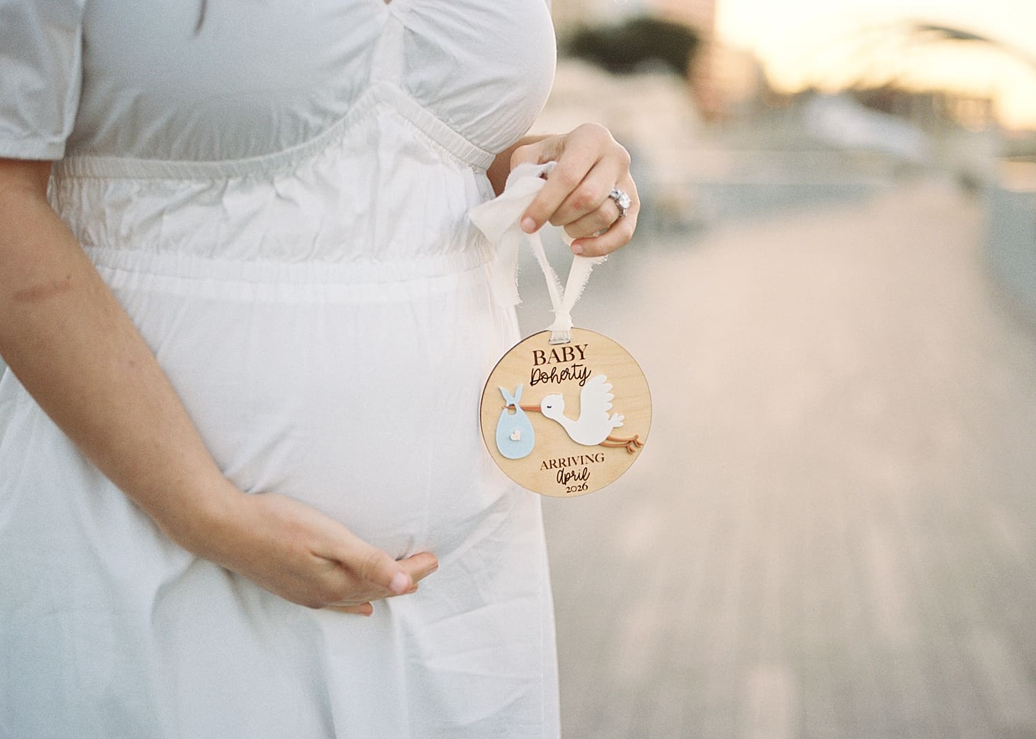 expectant mother in white dress holds baby bump and stork ornament