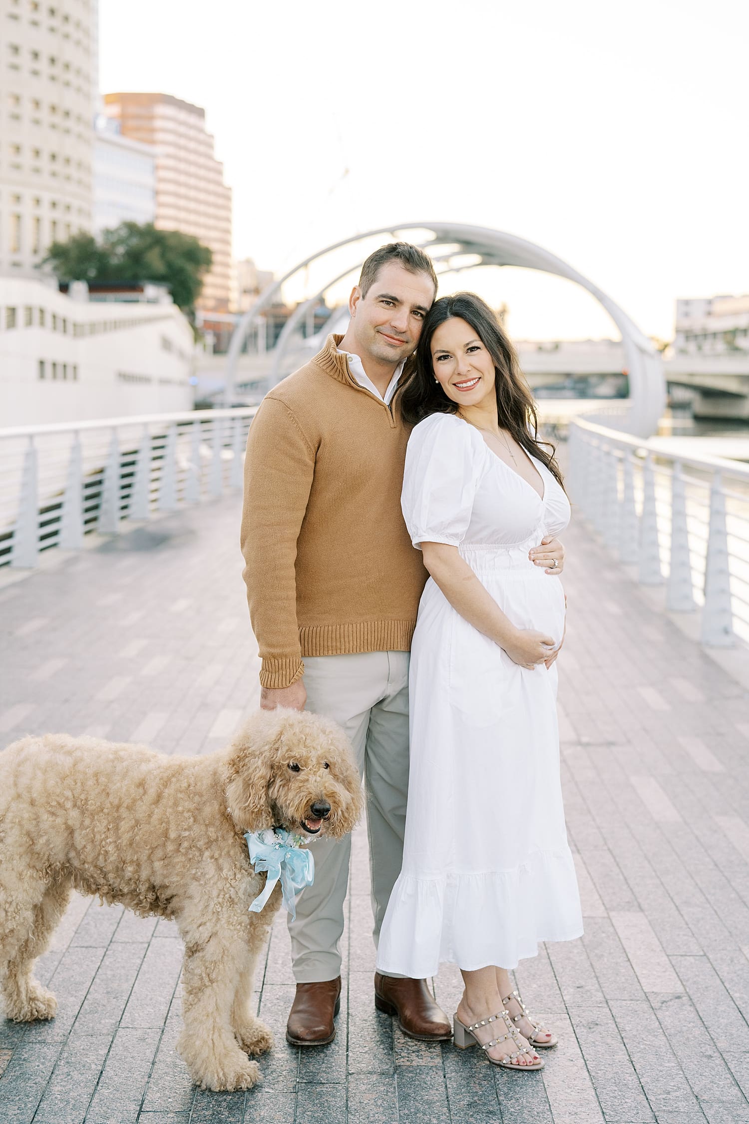 couple with their dog stand on riverwalk during matternity session