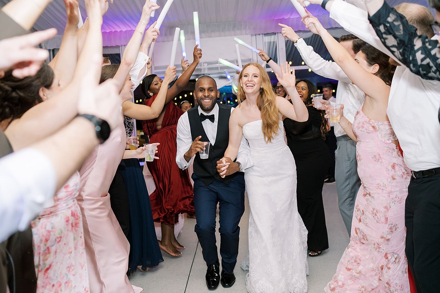 candid photos from wedding reception of bride and groom walking through tunnel of guests with arms raised