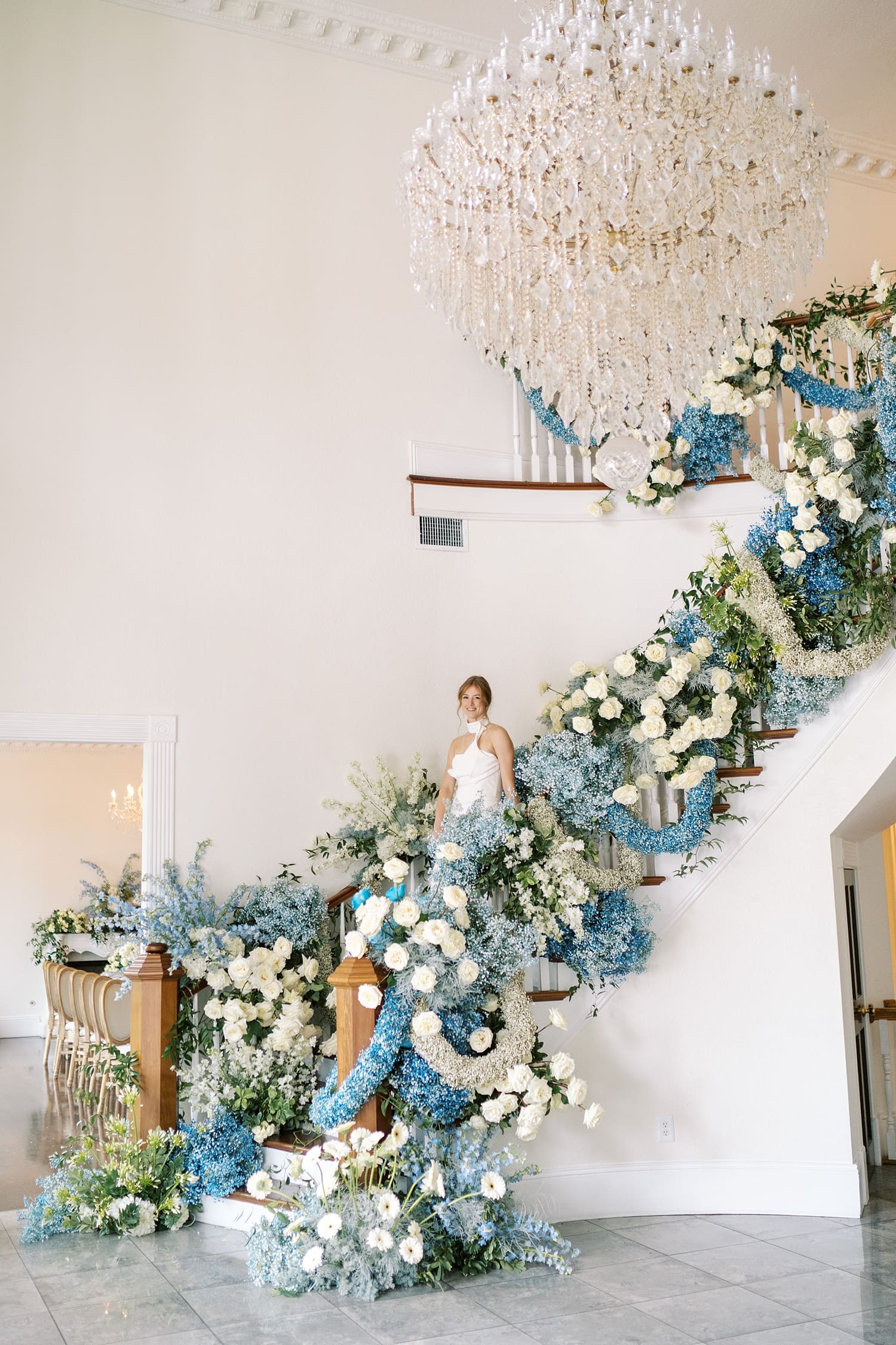 bride walks down grand staircase of Luxmore Grande Estate covered in white and blue florals creating a dramatic effect