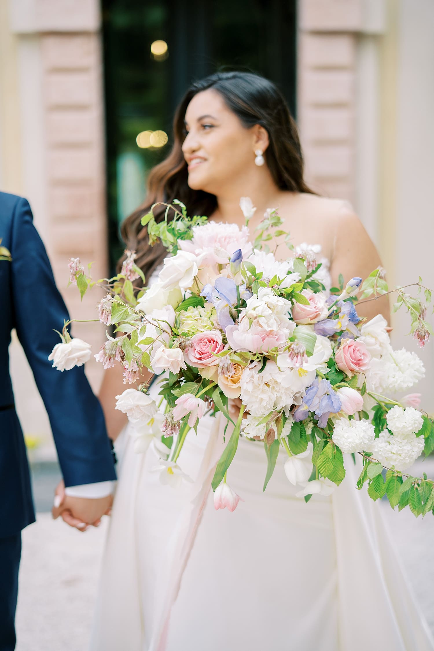 newlyweds walk together holding hands as bride carries romantic and organic bridal bouquet