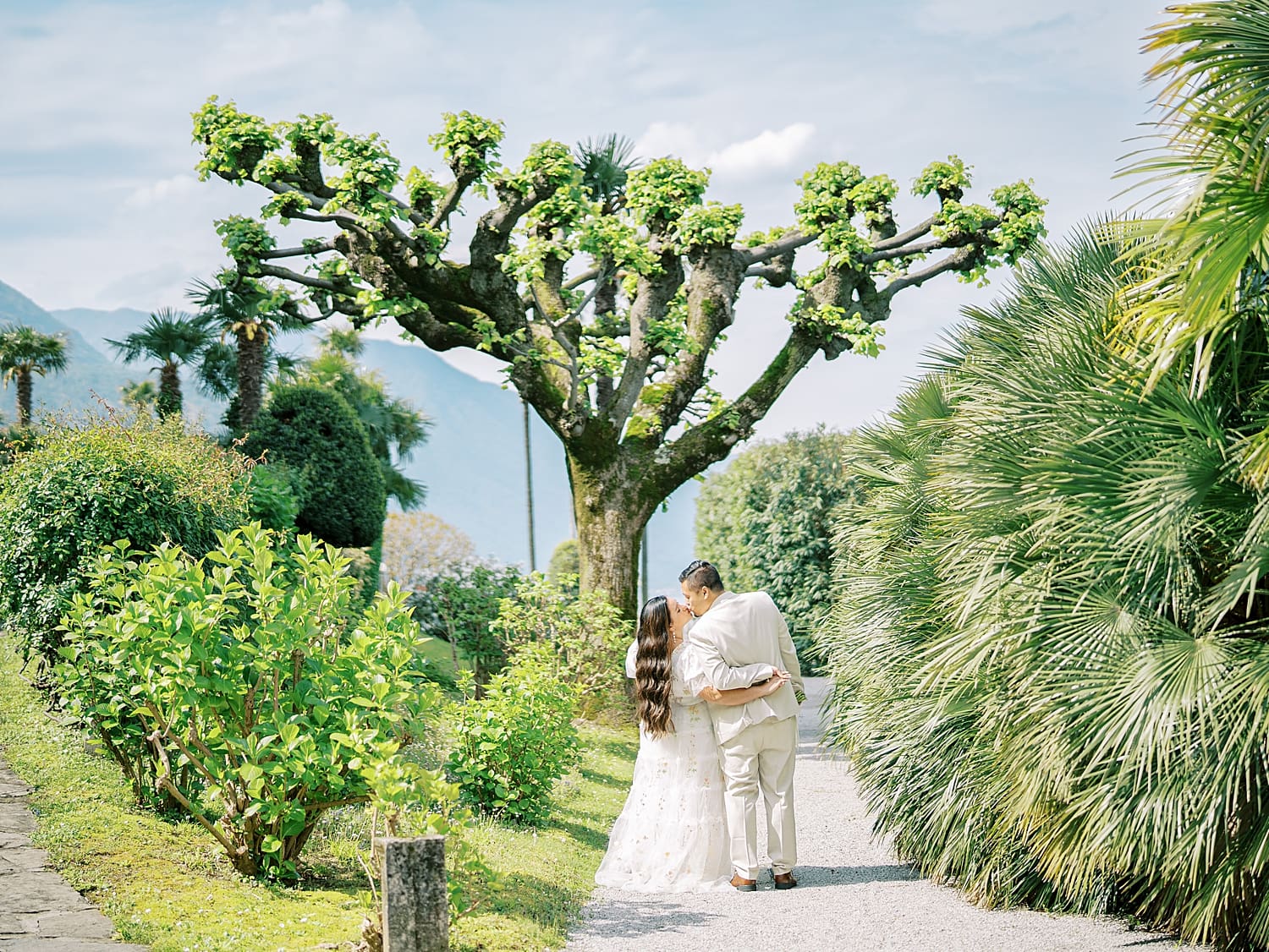 couple kiss on pathway surrounded by lush greenery at Villa Serbelloni